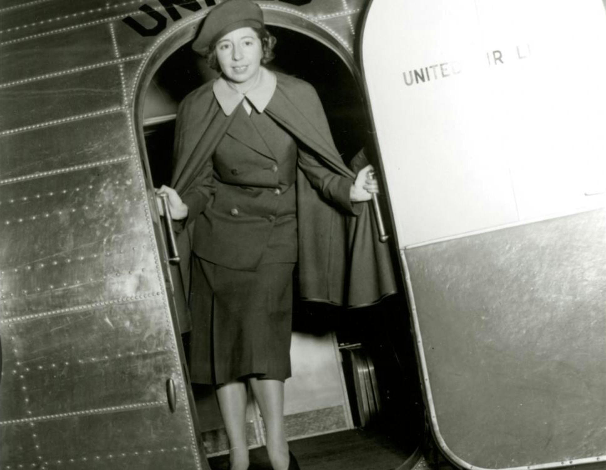 black and white photo of a female flight attendant standing at an open airplane door