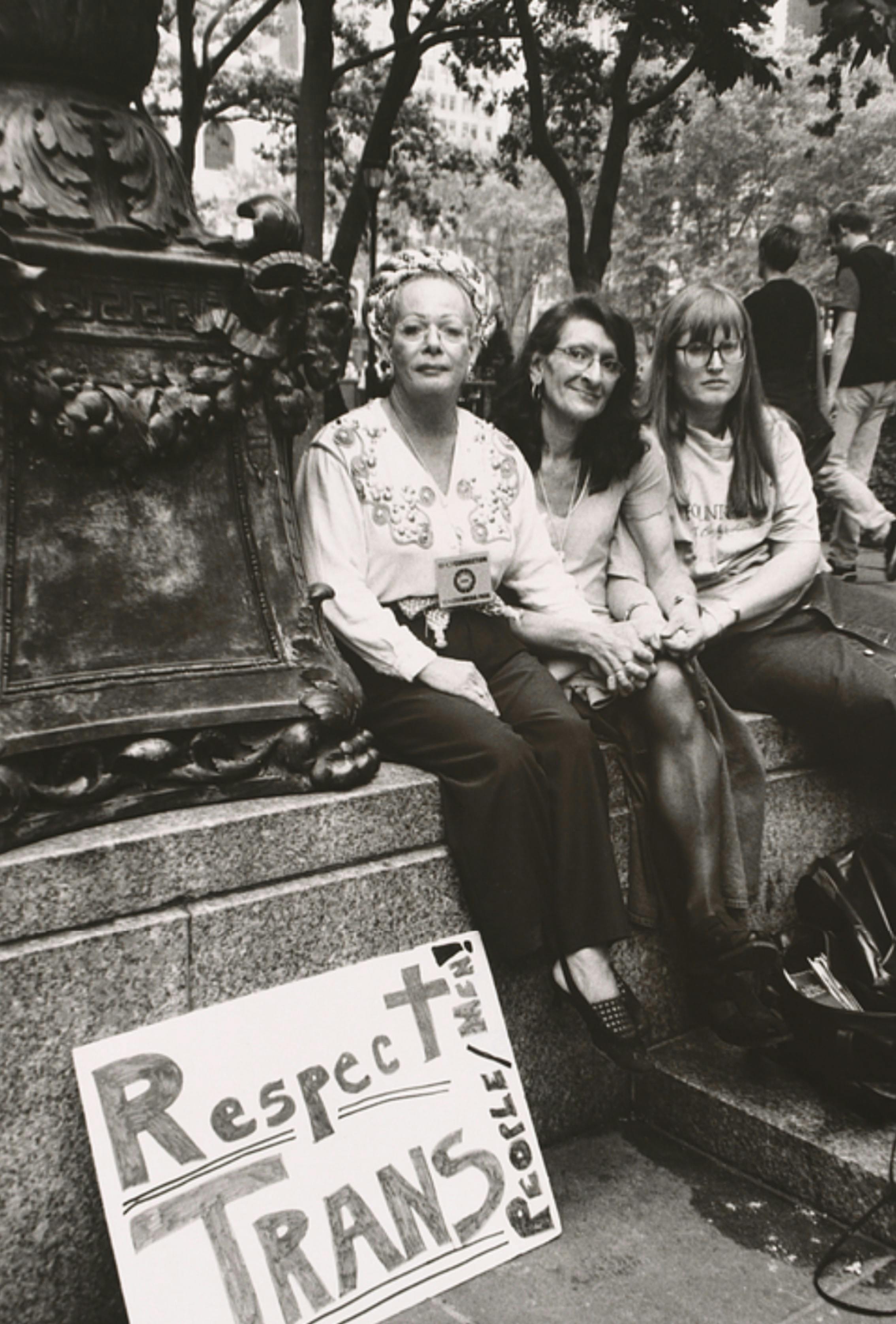 Sylvia Rivera, Christina Hayworth and Julia Murray sit on a ledge in a park in New York City. A sign near them reads: Respect Trans People/Men!