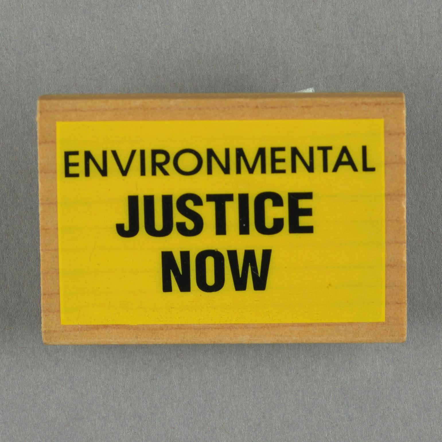 square wooden button with black text on yellow background. Text reads "Environmental Justice Now"