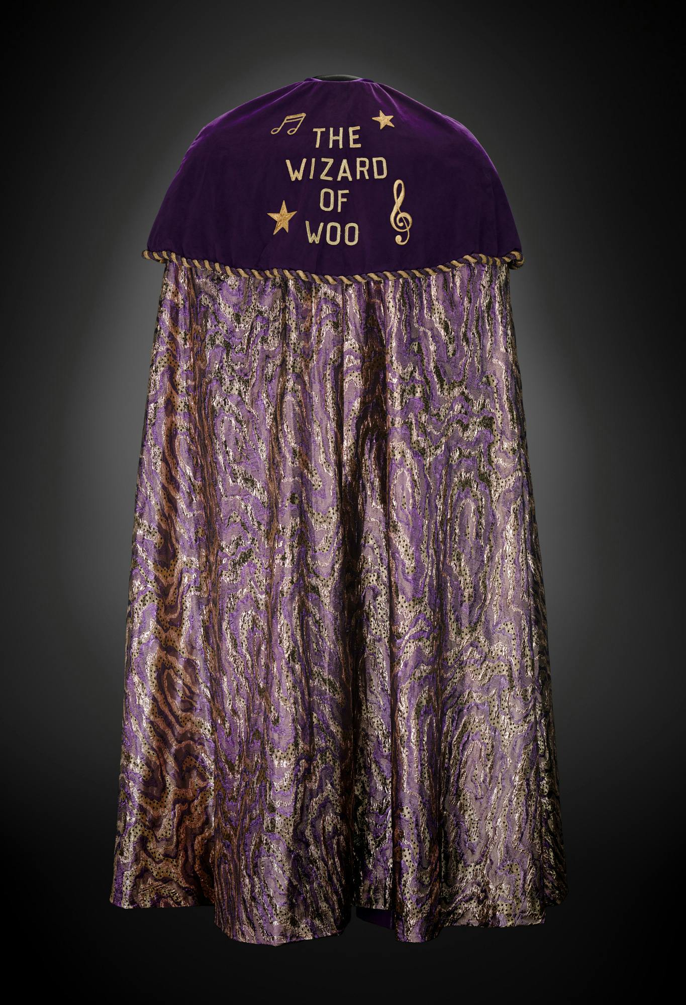 a purple cape with gold musical notes and stars stitched in and the words "The Wizard of Woo"