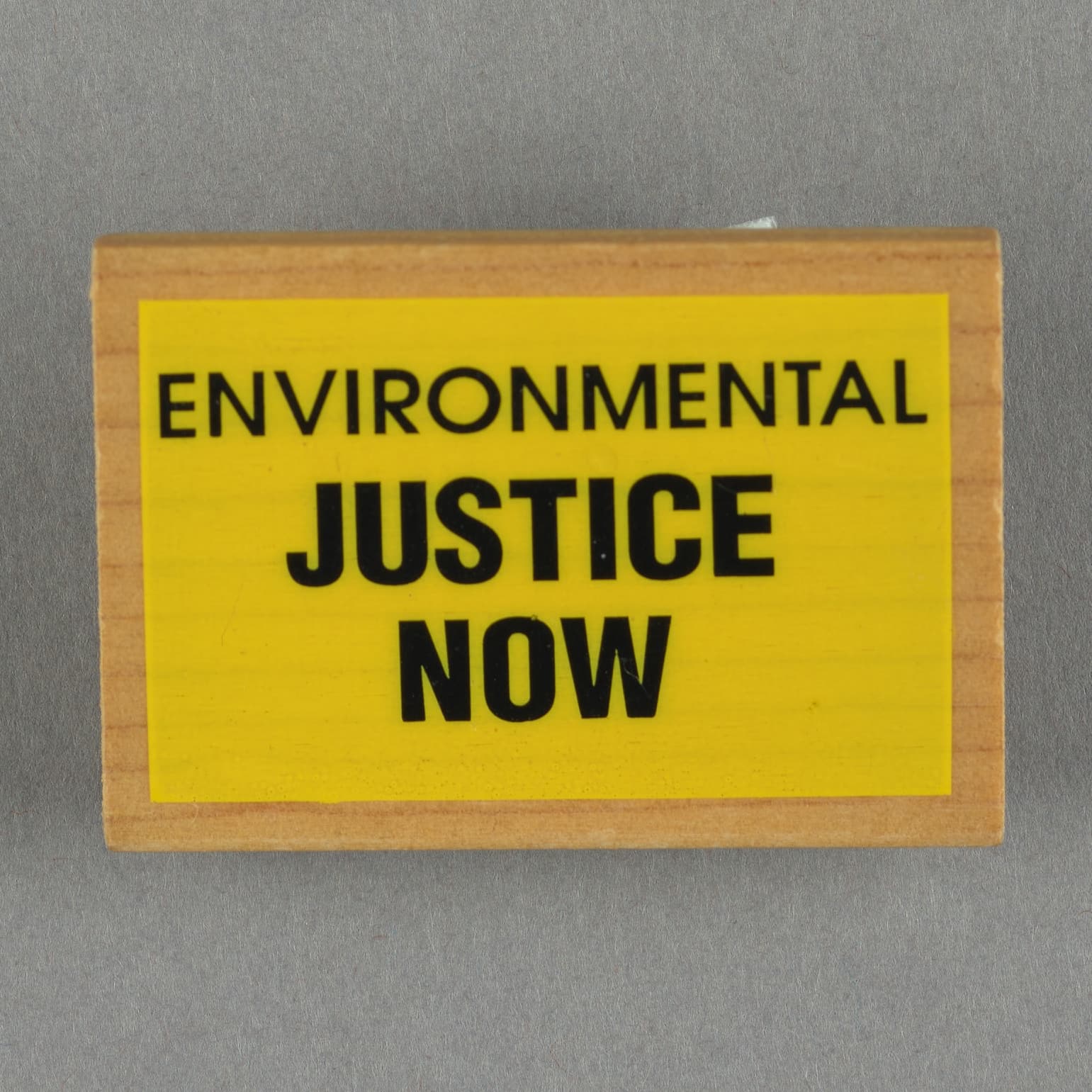 square wooden button with black text on yellow background. Text reads "Environmental Justice Now"